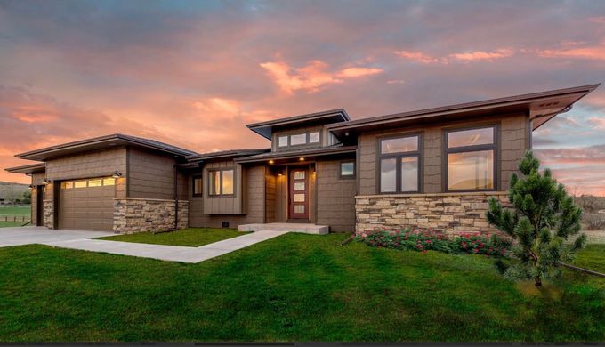 Modern brown house with stone accents and a green lawn under a colorful sunset.