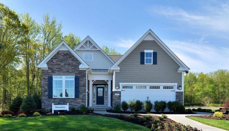 Cottage-style home with stone and gray siding, blue shutters, and a white garage door under a bright blue sky.