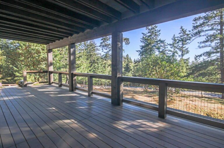 Wooden deck overlooking a forest, brown railings, and beams, blue sky.