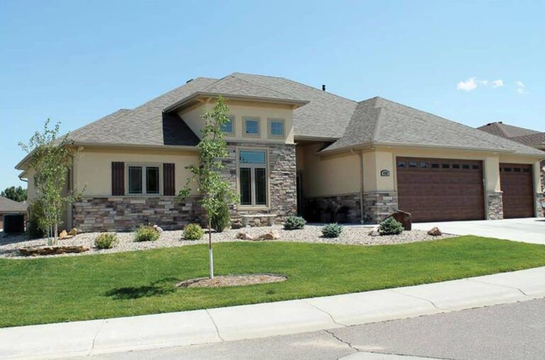 Tan and stone home with a brown garage door, manicured lawn, and blue sky.