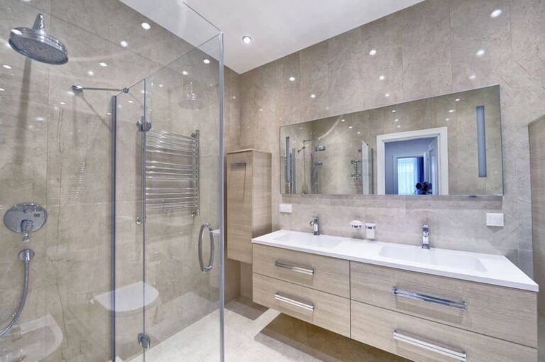 Modern bathroom with a glass shower, double vanity, and beige tiled walls.
