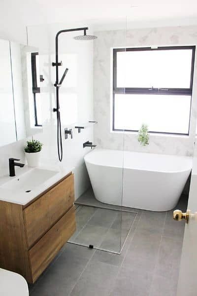 Modern white bathroom with a wooden vanity, soaking tub, and black fixtures.