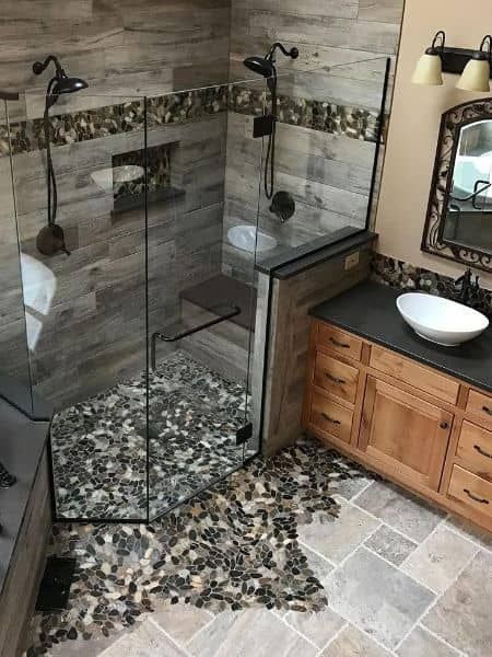 Bathroom with a glass shower, pebble floor, dual shower heads, and wooden vanity.