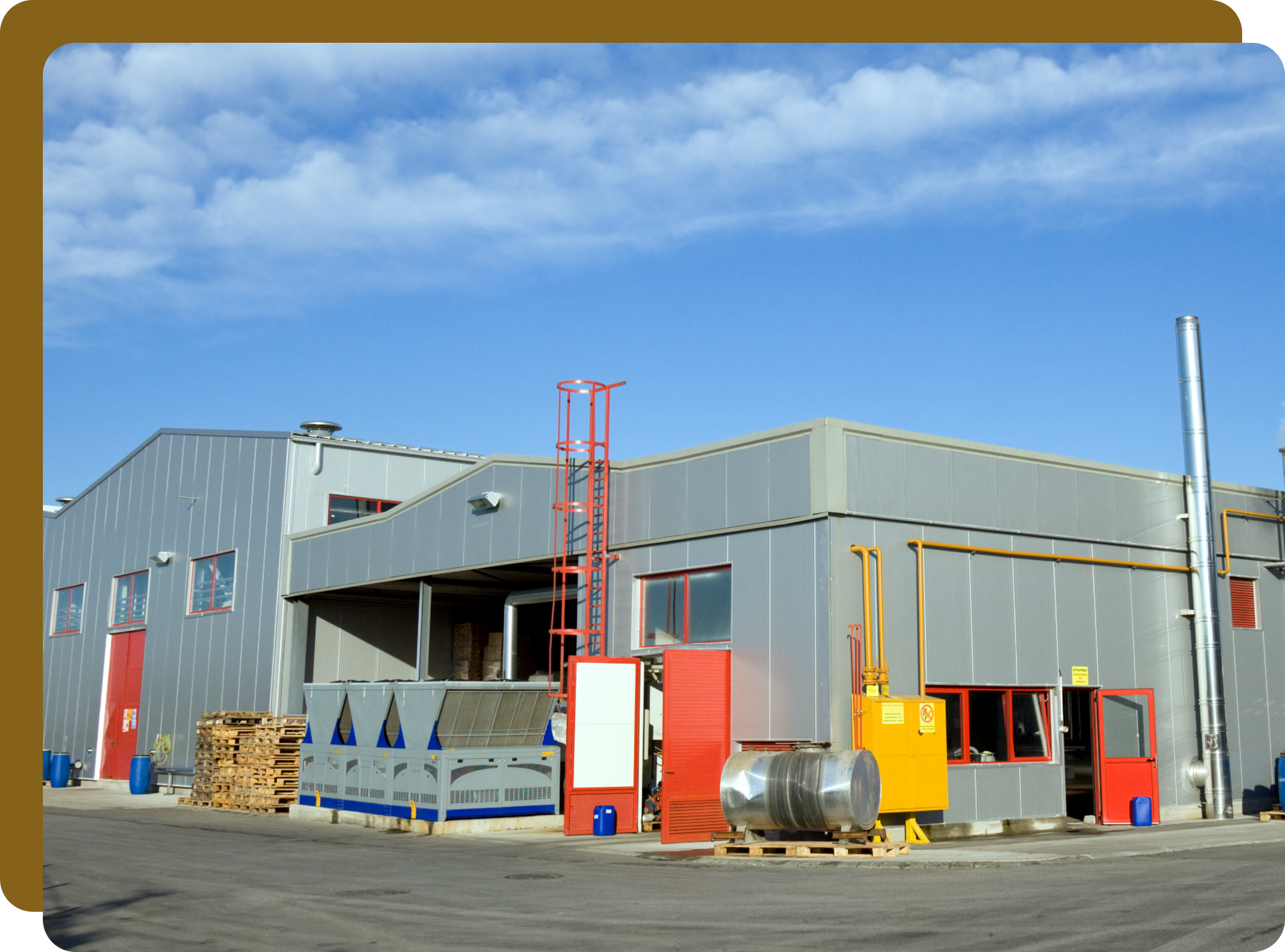 Industrial building exterior, gray metal siding, blue sky, various machinery and equipment outside.
