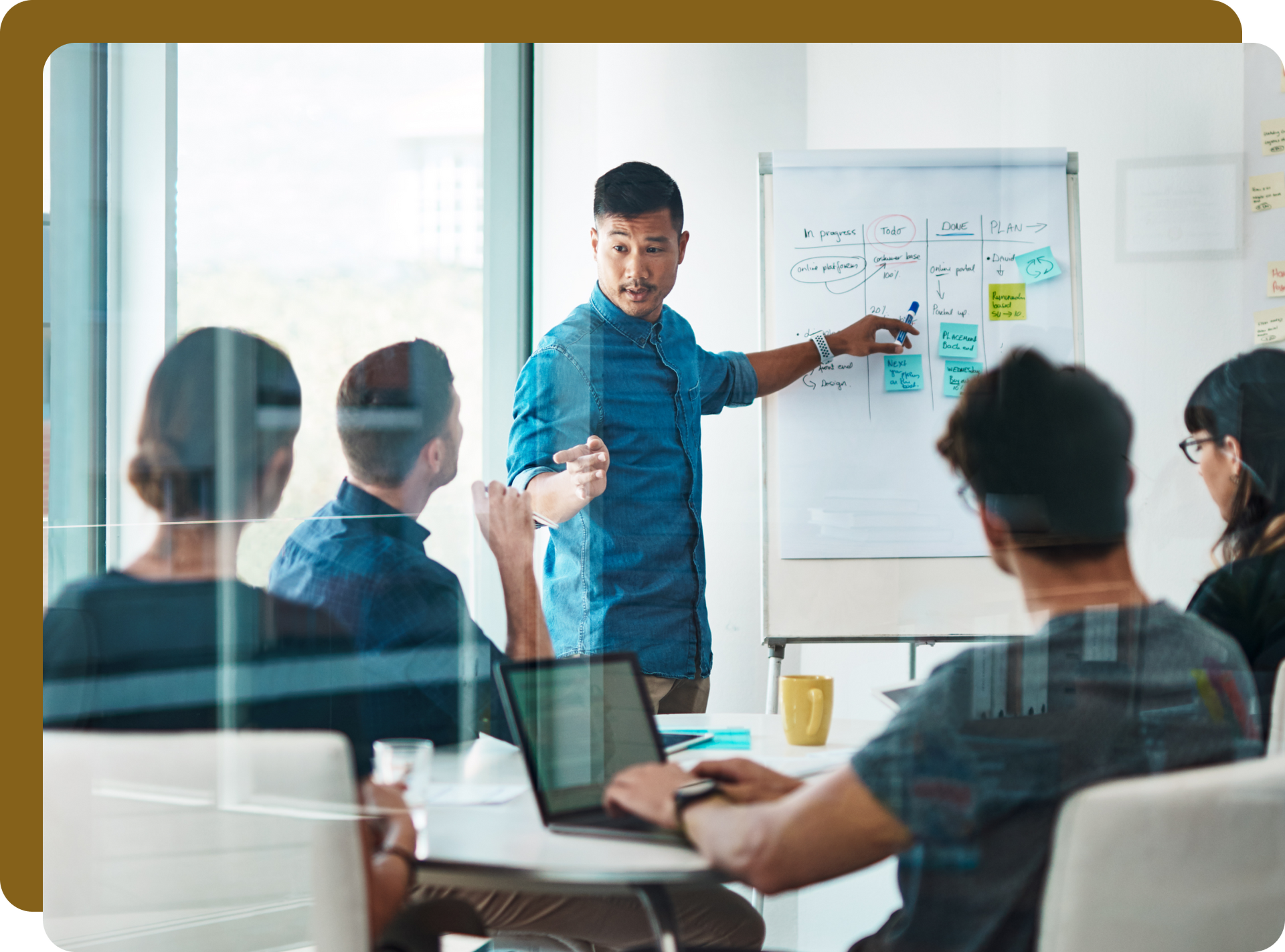 Asian man presenting to colleagues at whiteboard in modern office.