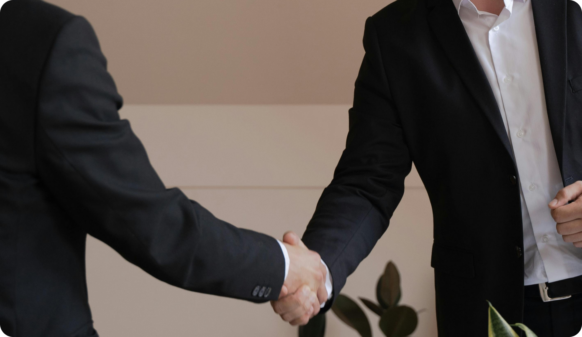 Two men in suits shaking hands, indoors.