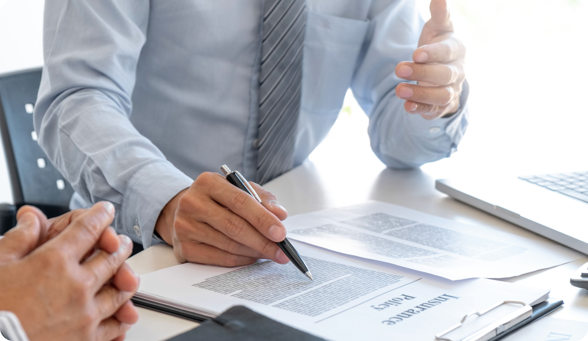 Two men at a table reviewing documents; one points and holds a pen, discussing with the other.