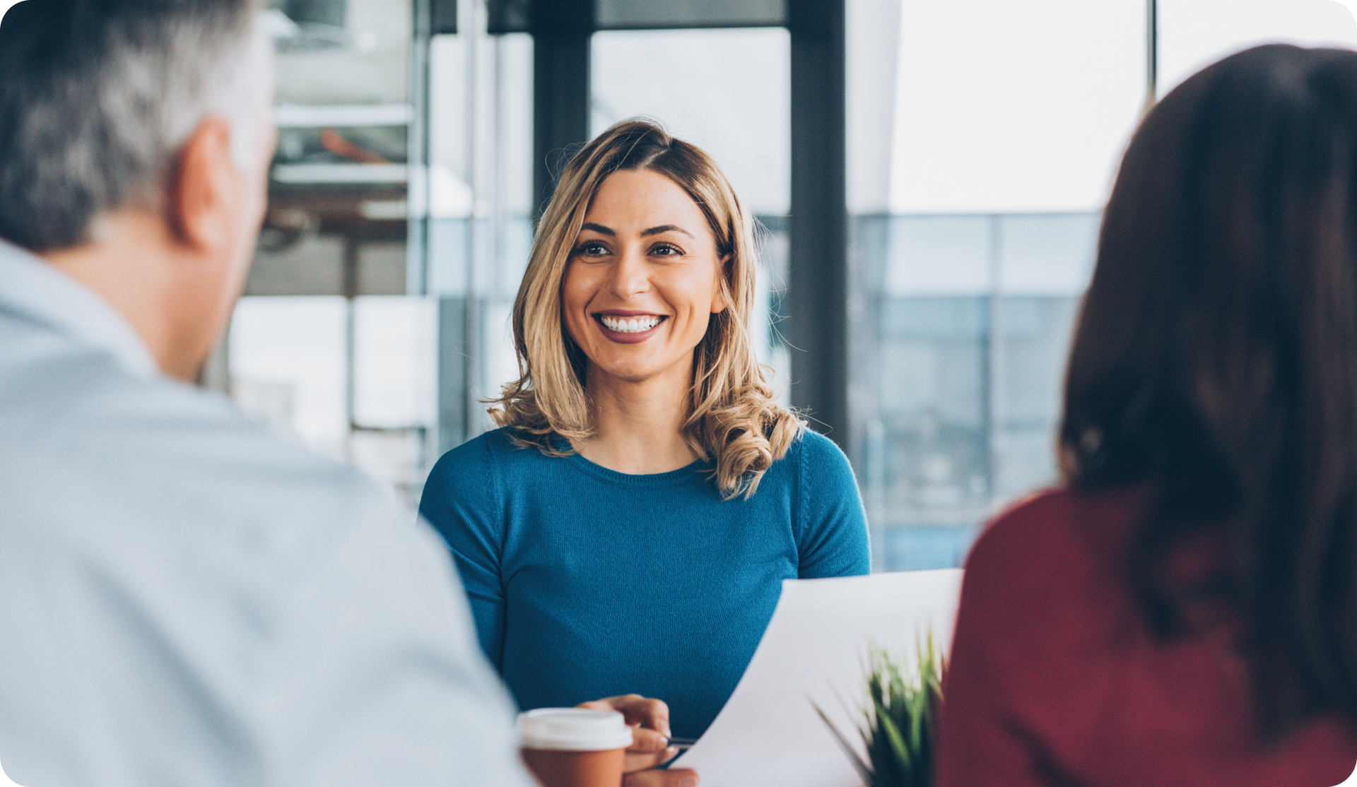 Woman smiles at a couple during a meeting in a modern office setting.