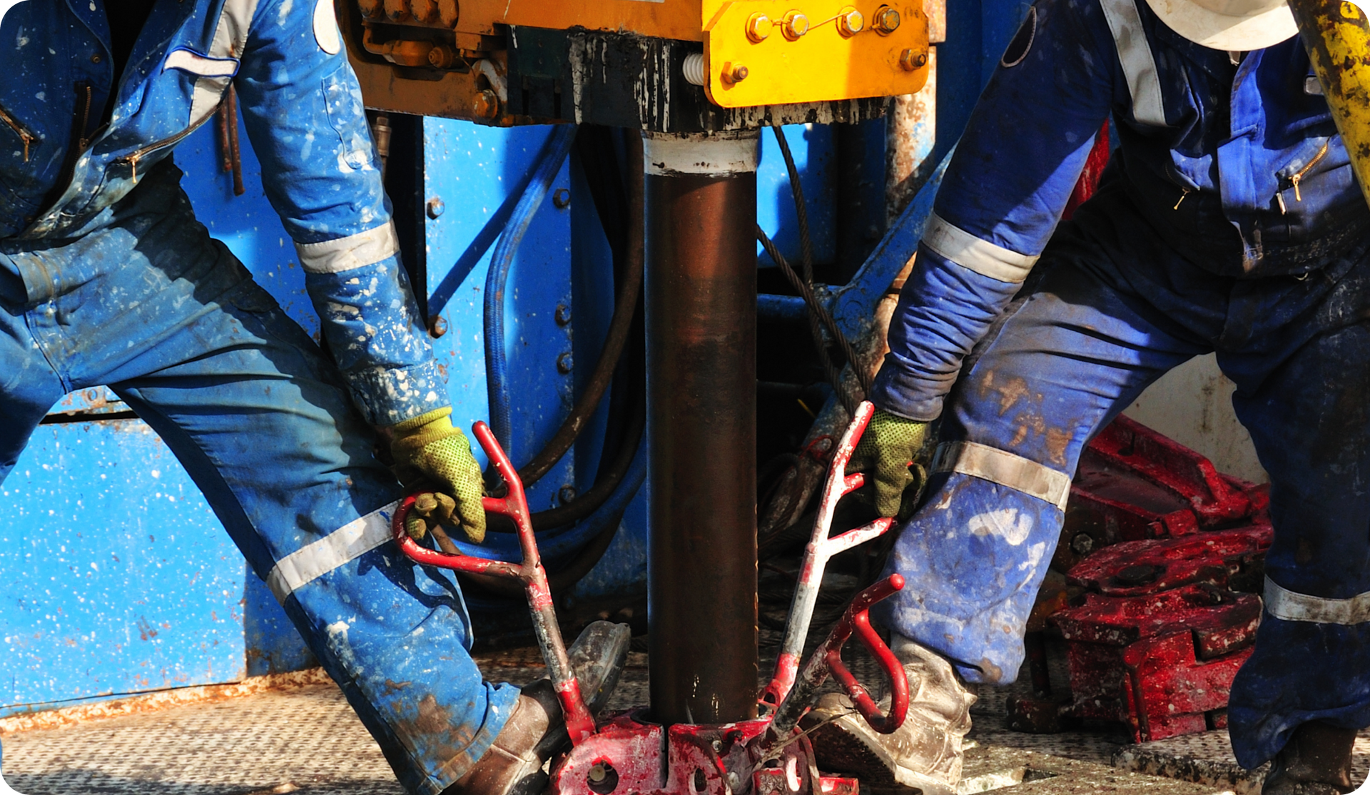 Workers in blue coveralls operating machinery at a drilling site.