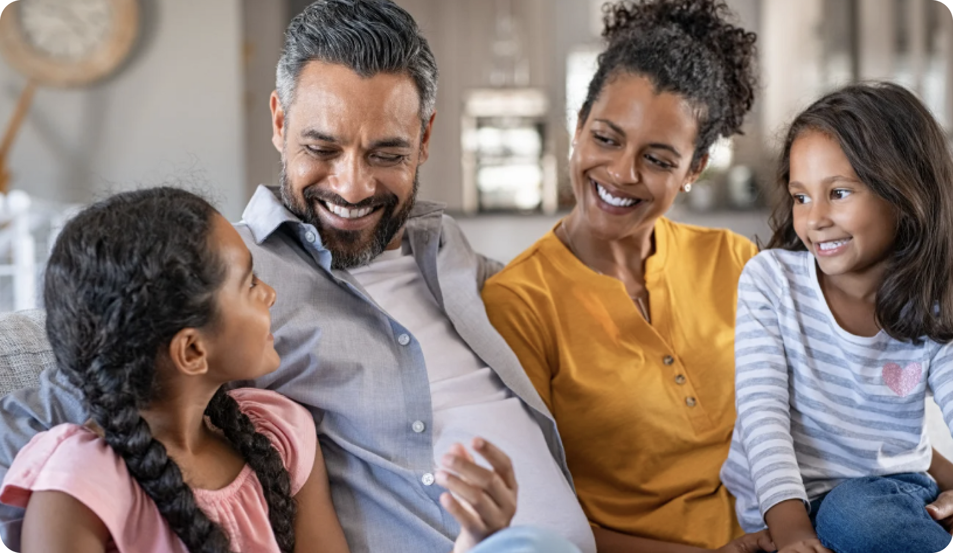 Family of four smiling on a sofa indoors: a man, woman, and two young girls.