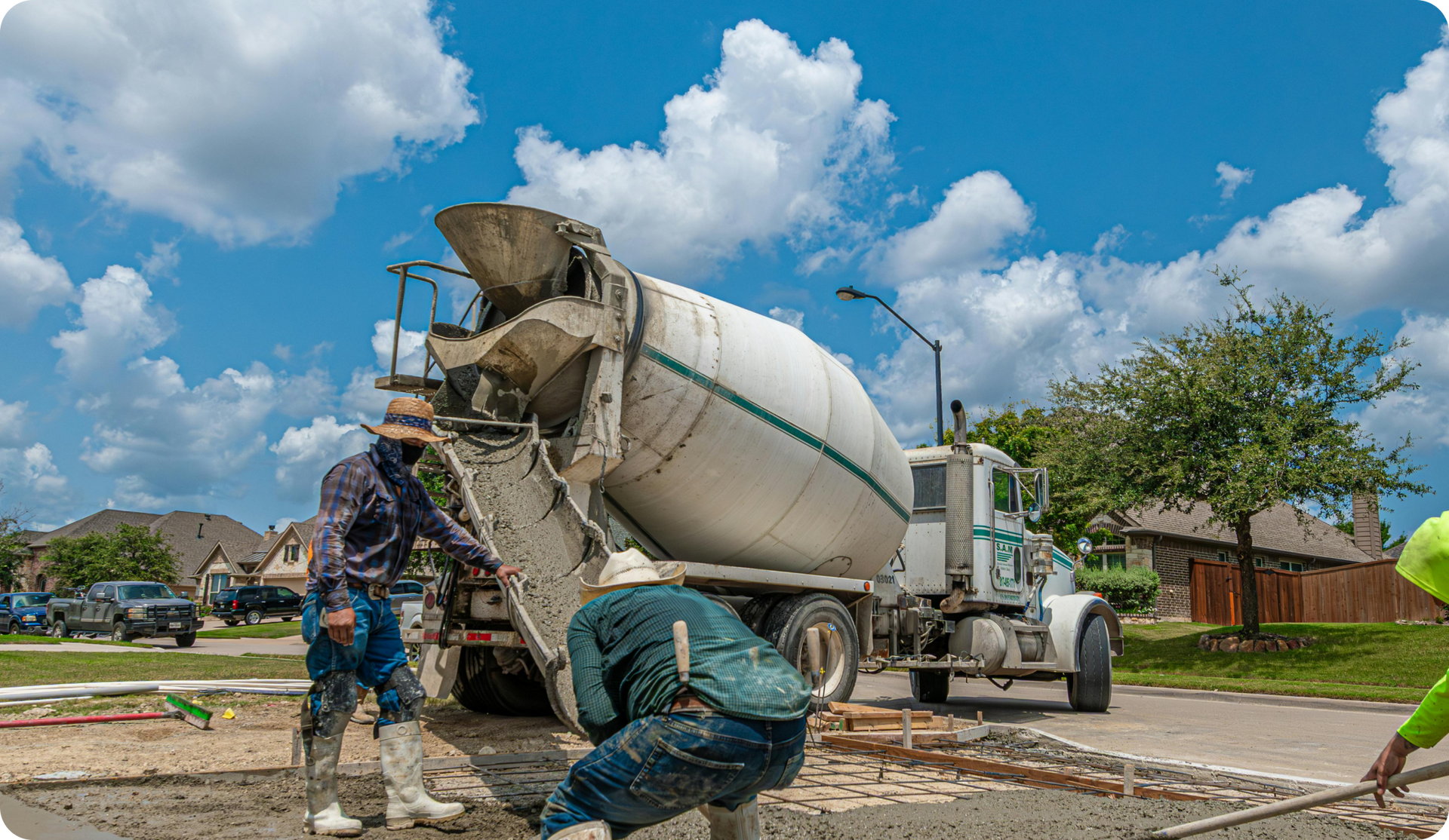 Concrete truck pouring cement on a construction site; workers in protective gear. Blue sky.