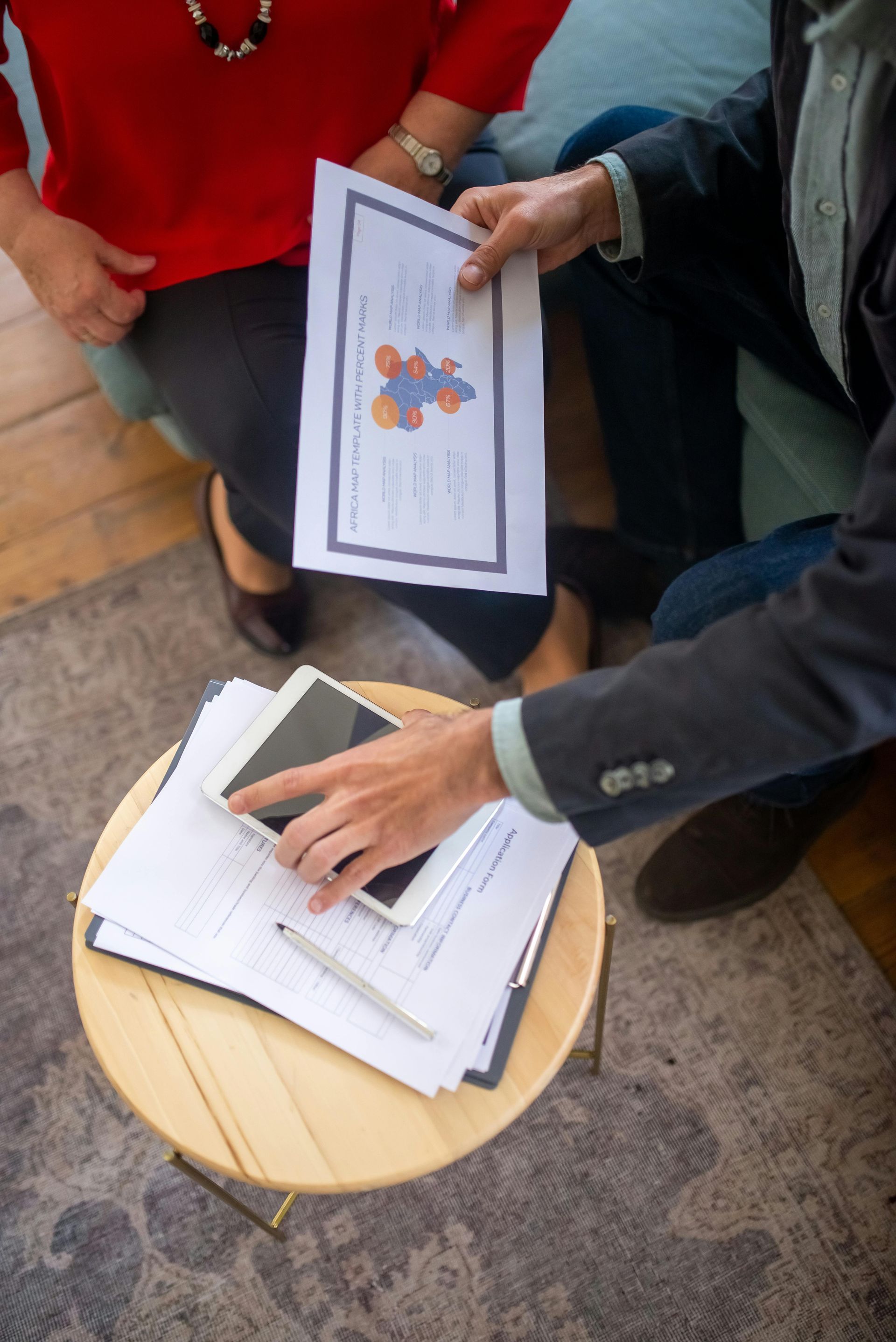 A man and a woman are sitting on a couch looking at papers and a tablet.