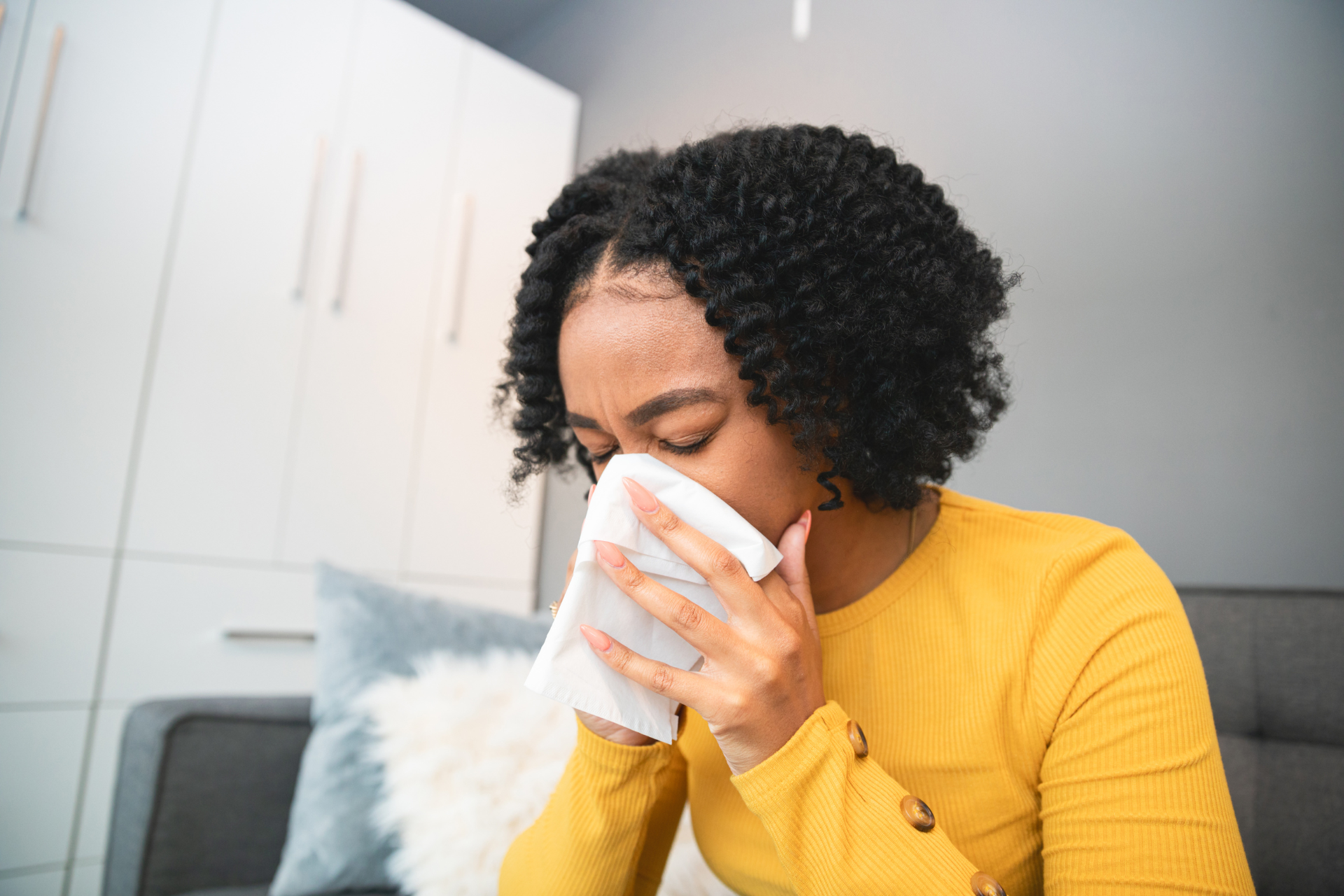A woman is blowing her nose into a napkin while sitting on a couch.