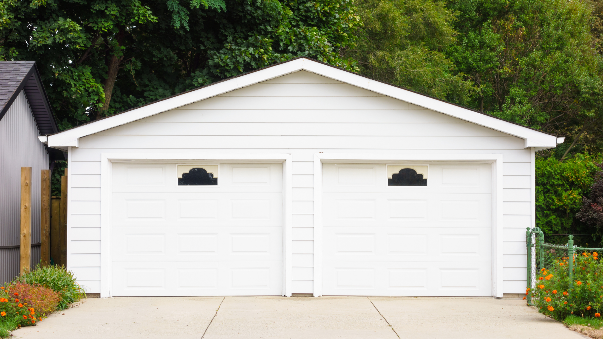 White two-car garage with black arched windows; concrete driveway. Green foliage in the background.