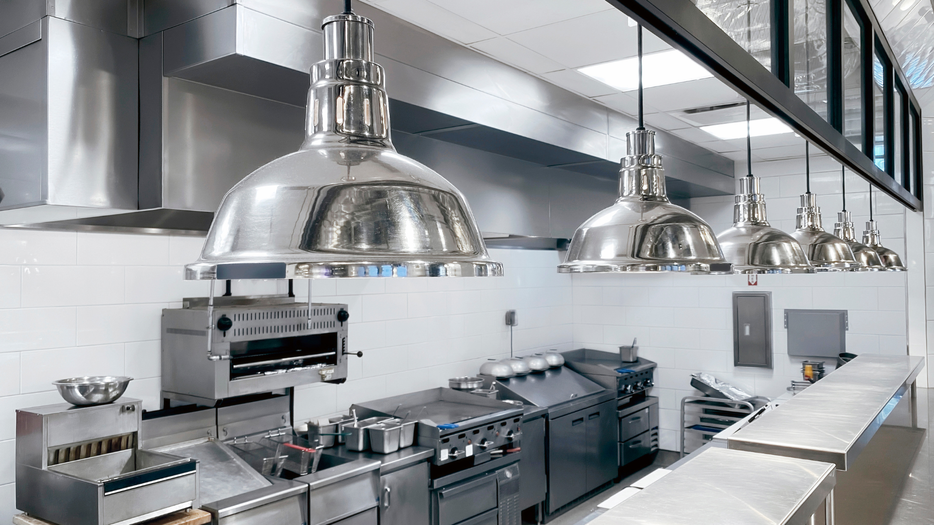 A commercial kitchen with stainless steel appliances, bright overhead lights, and a long countertop.