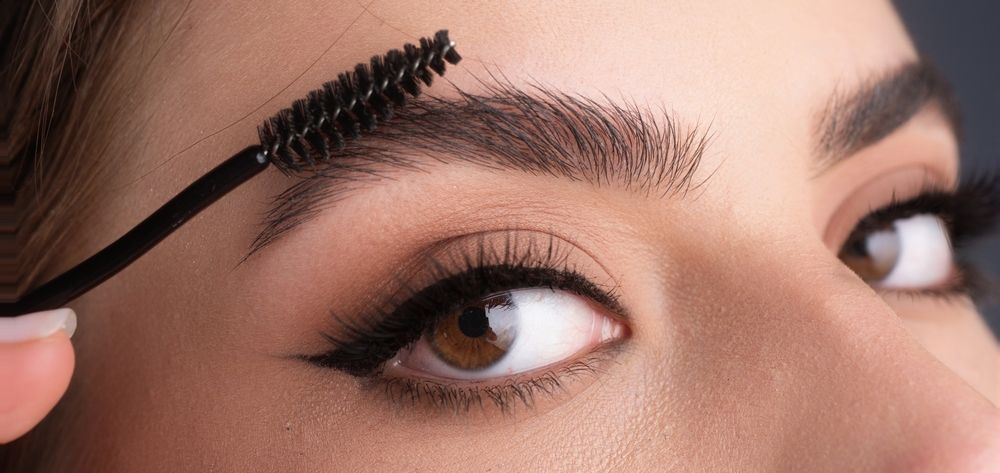 A woman is brushing her eyebrows with a brush.