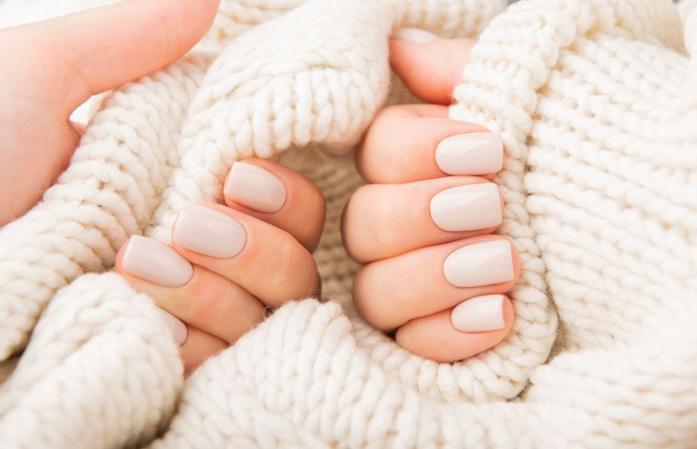 A woman 's hands with white nails are wrapped in a white sweater.