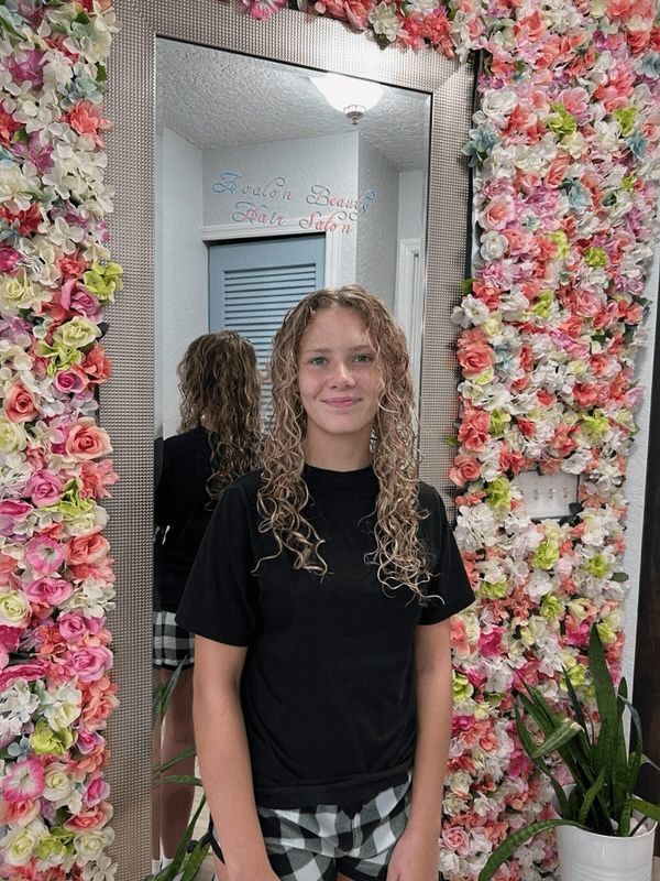 A woman is standing in front of a mirror in front of a wall of flowers.