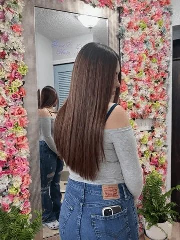 A woman is standing in front of a mirror in front of a wall of flowers.