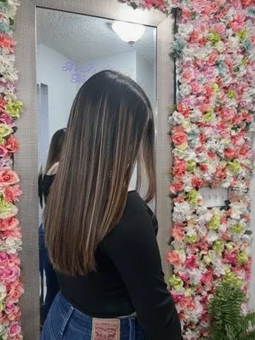 A woman is standing in front of a mirror in front of a wall of flowers.