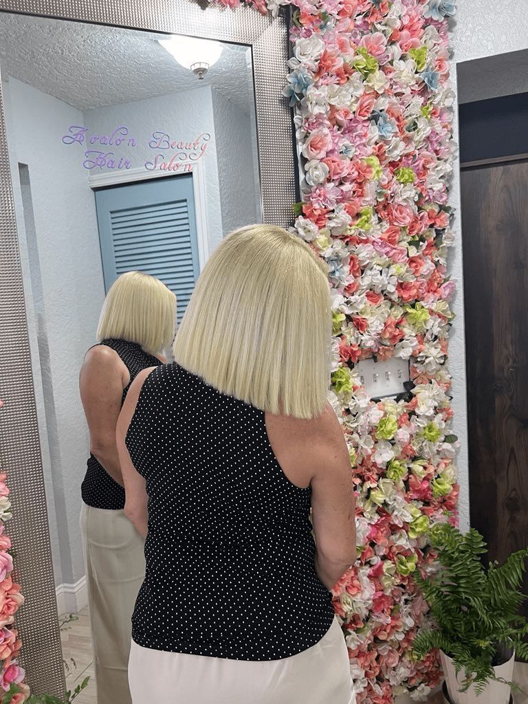 A woman is standing in front of a mirror with flowers on the wall behind her.