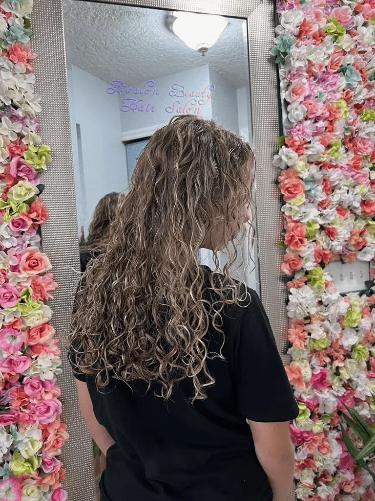 A woman is standing in front of a mirror in front of a wall of flowers.