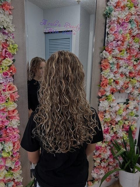 A woman with curly hair is standing in front of a wall of flowers.