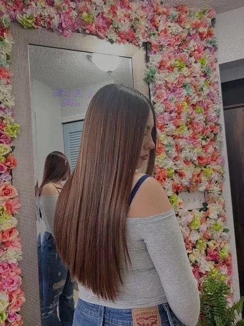 A woman is standing in front of a mirror in front of a wall of flowers.