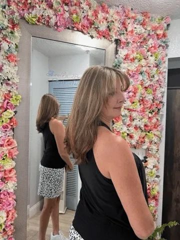A woman is standing in front of a mirror in front of a wall of flowers.