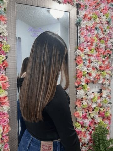 A woman is standing in front of a mirror in front of a wall of flowers.
