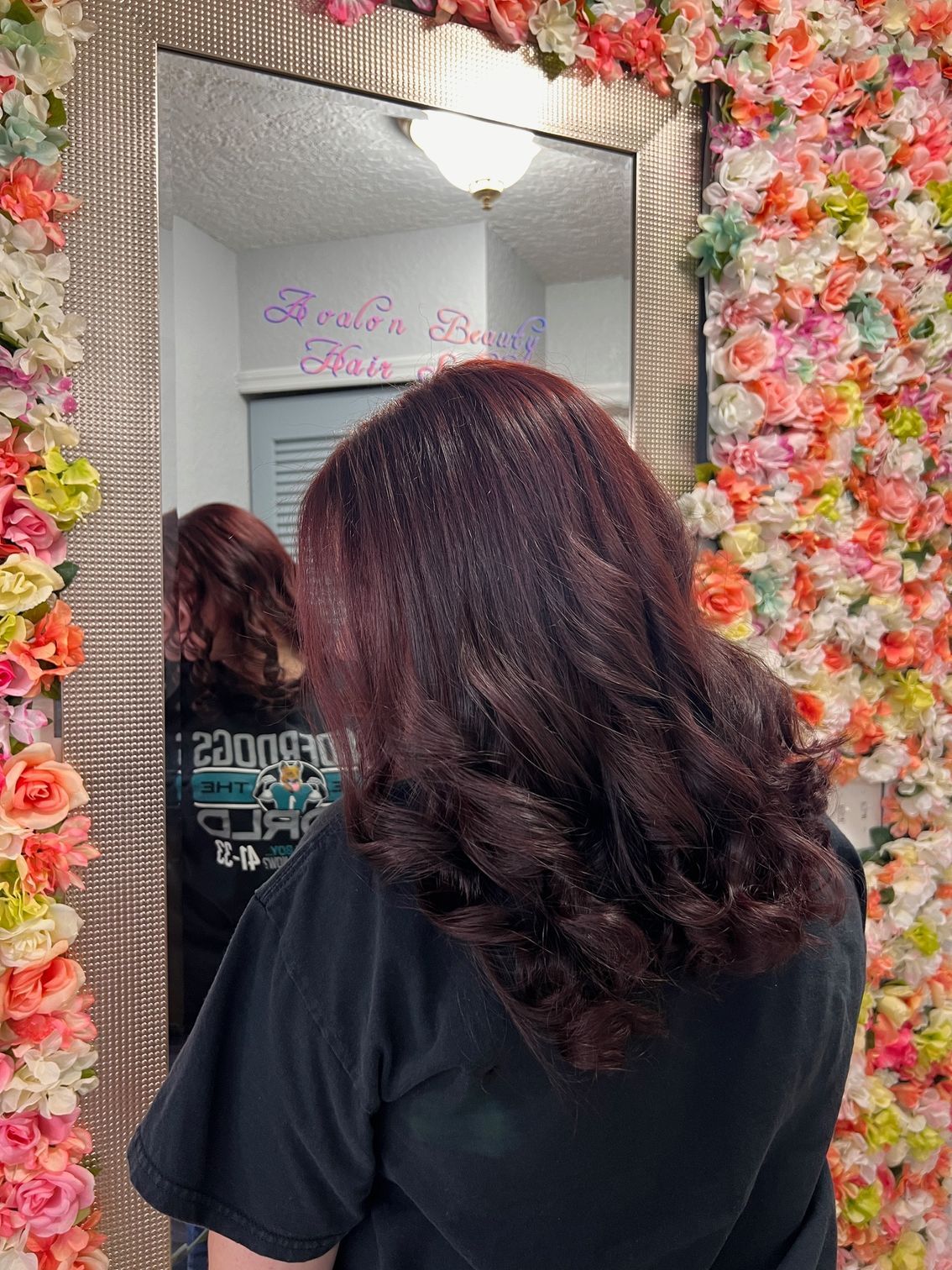 A woman is standing in front of a mirror in front of a wall of flowers.