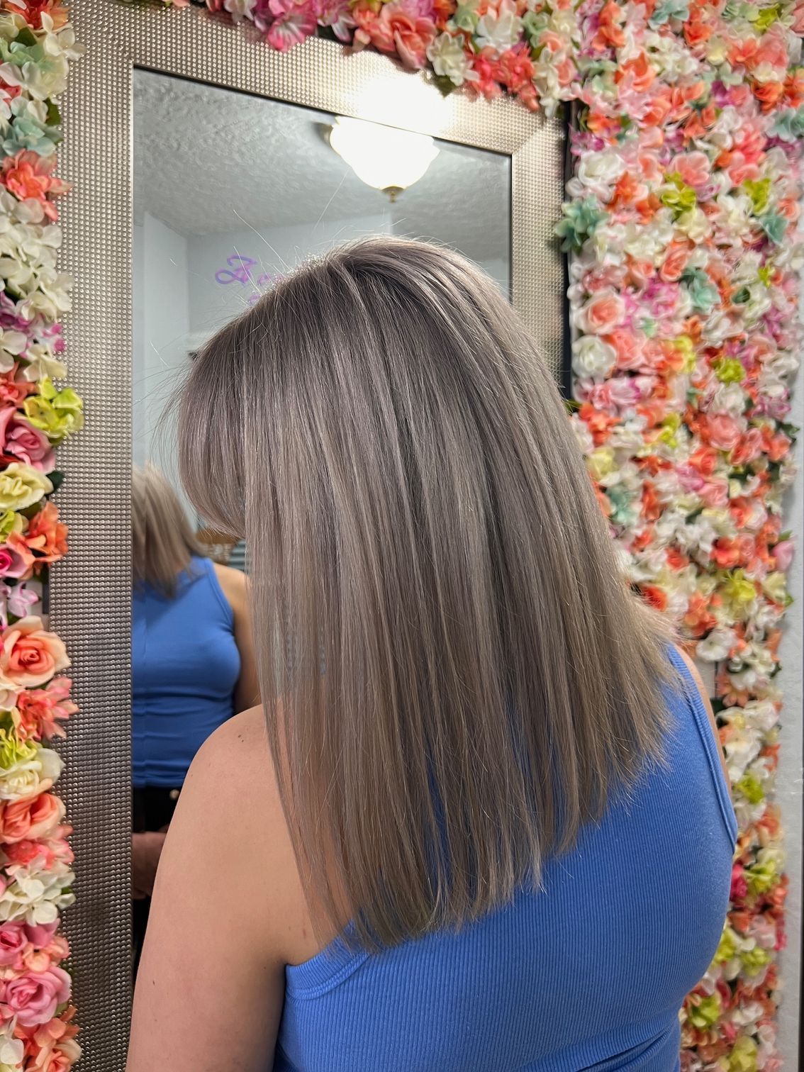 A woman is standing in front of a mirror with flowers on the wall behind her.