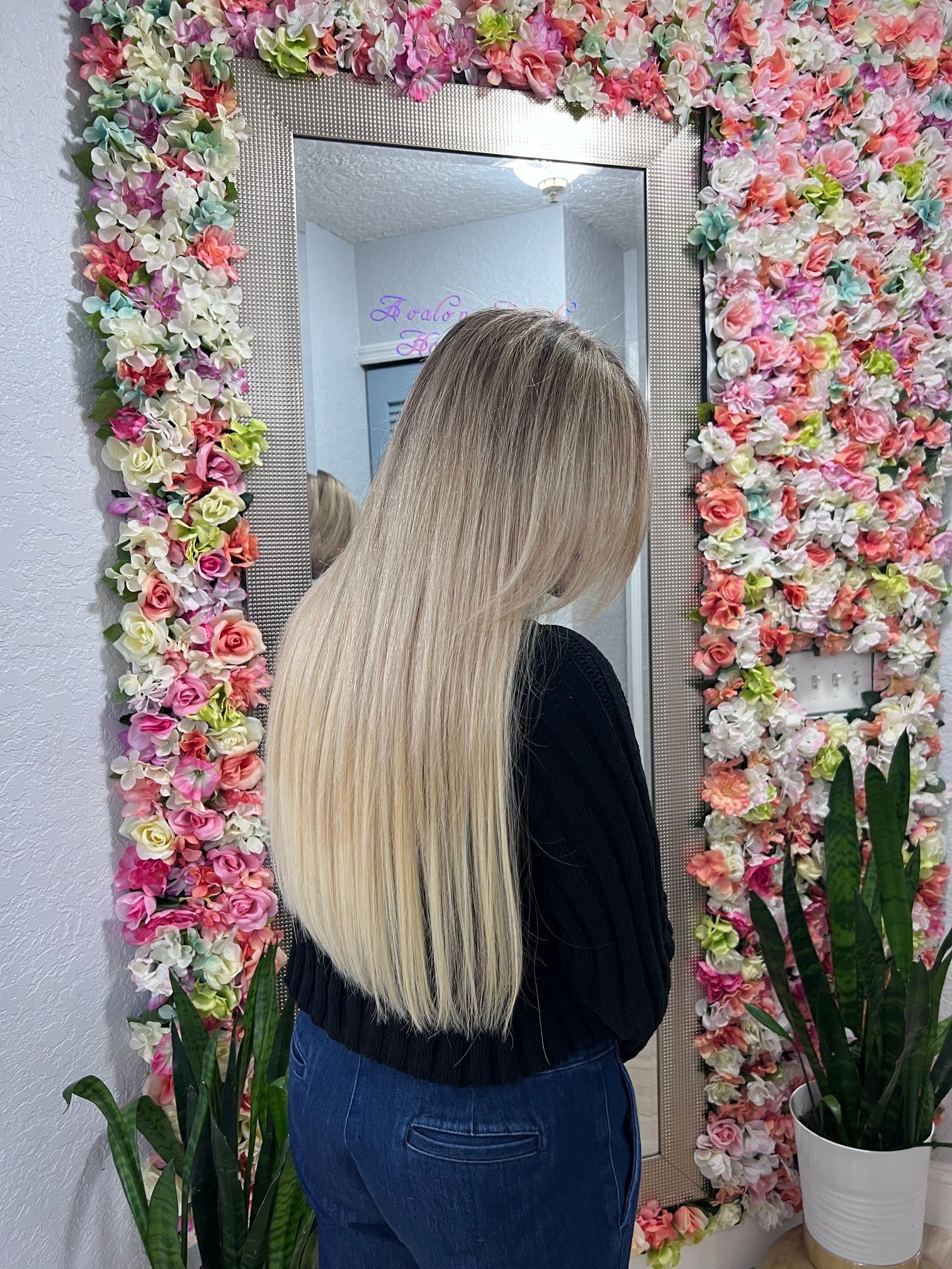 A woman is standing in front of a mirror surrounded by flowers.