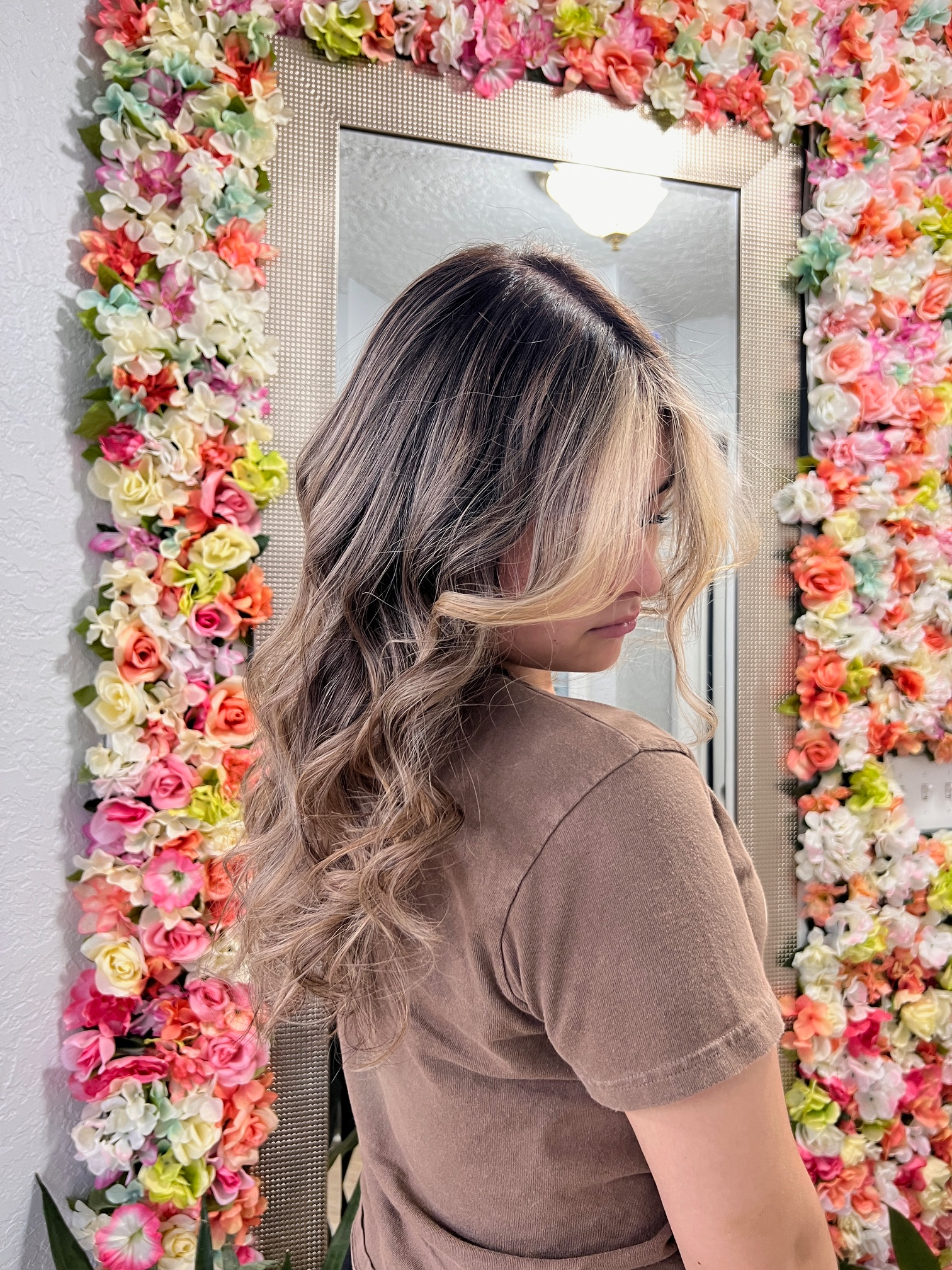 A woman is standing in front of a mirror surrounded by flowers.