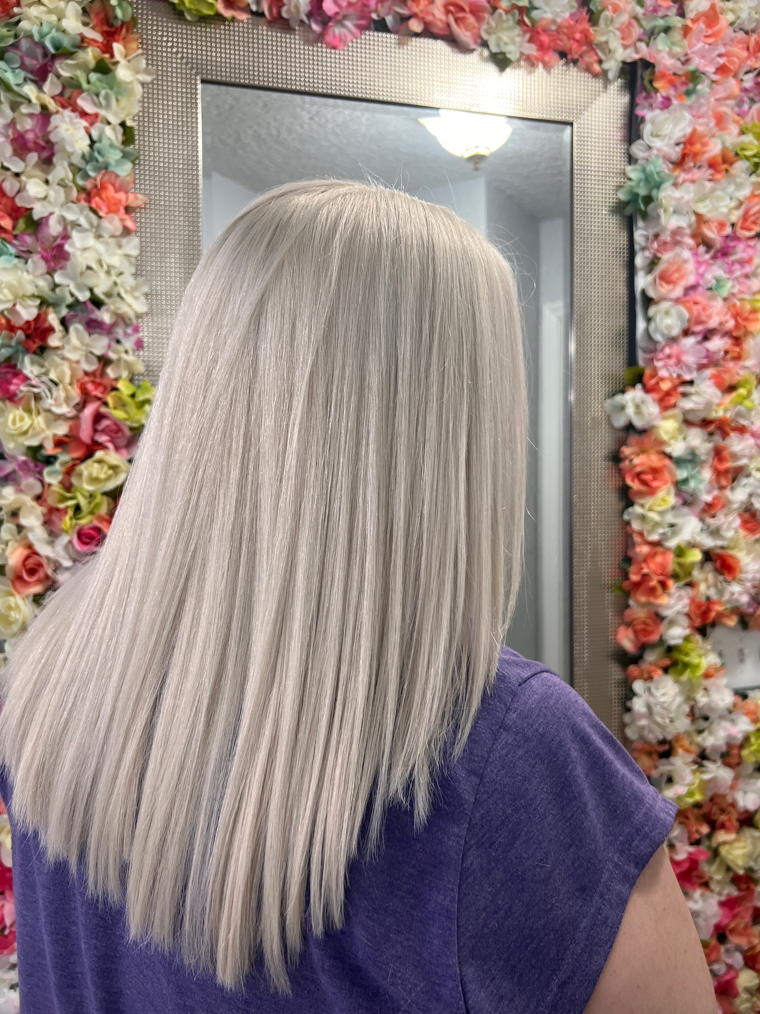 A woman standing in front of a mirror with flowers on the wall behind her