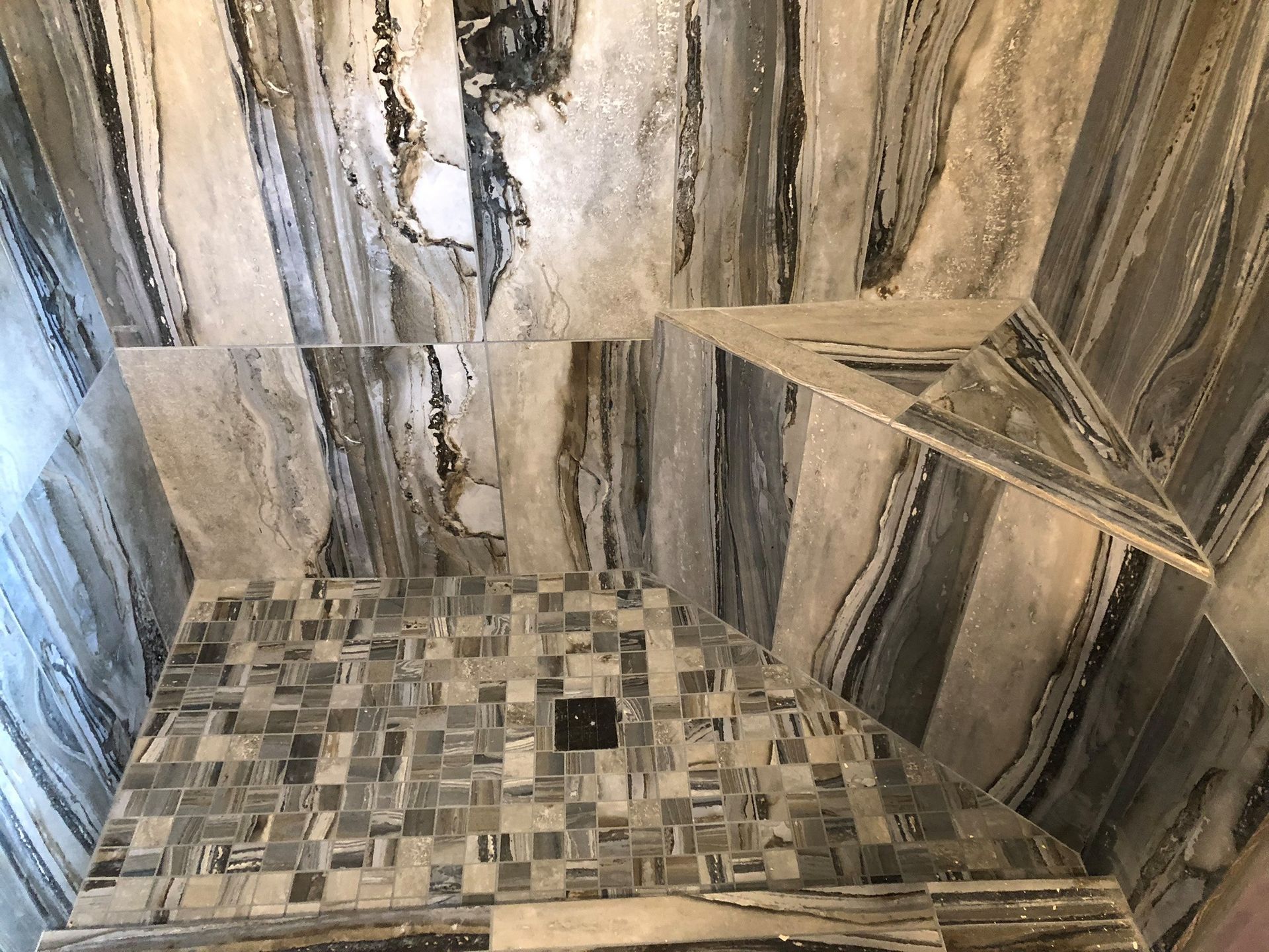 A shower stall with a tiled floor and a marble wall.