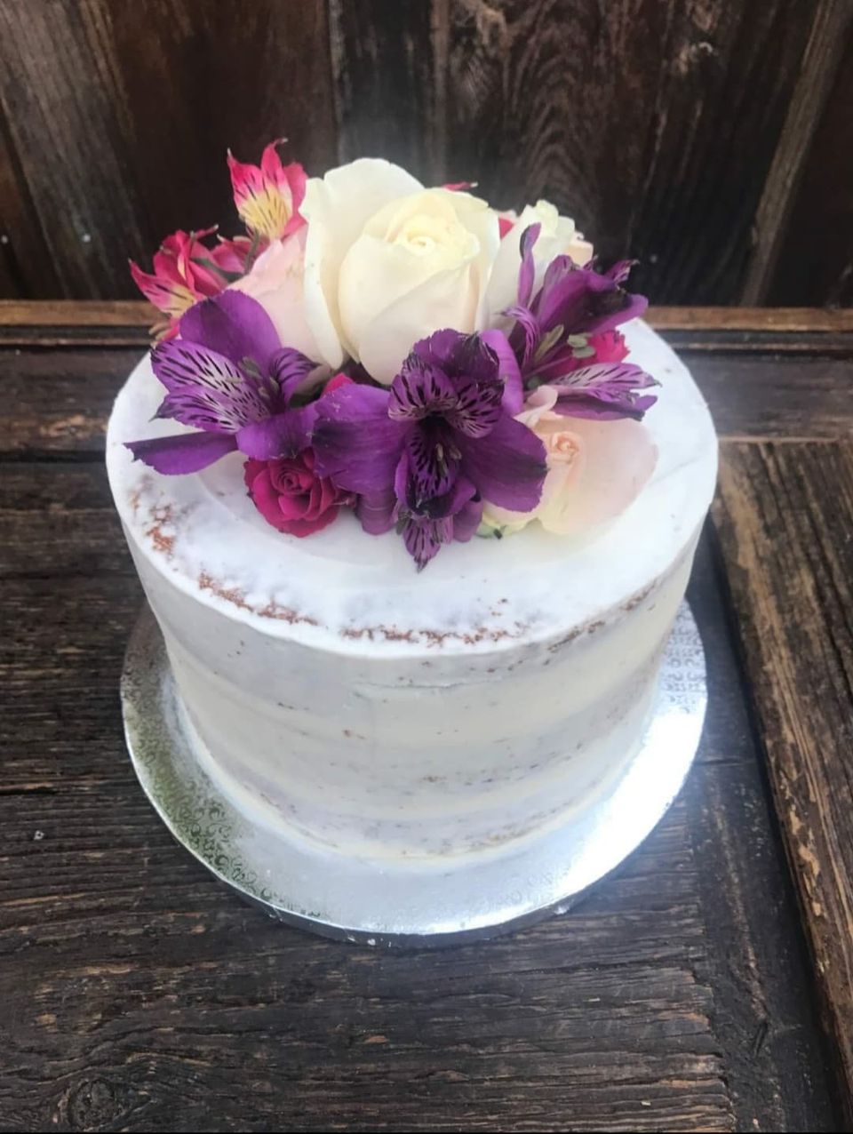 Cake with white frosting and fresh purple and pink flowers on top.