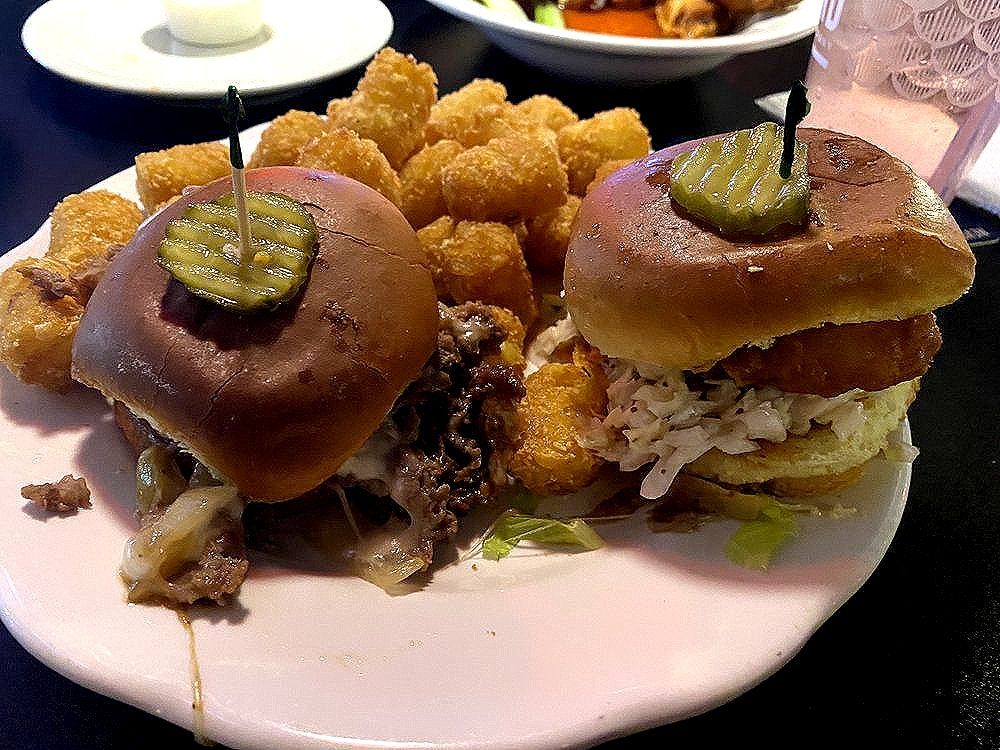 A plate of food with hamburgers and tots on a table.