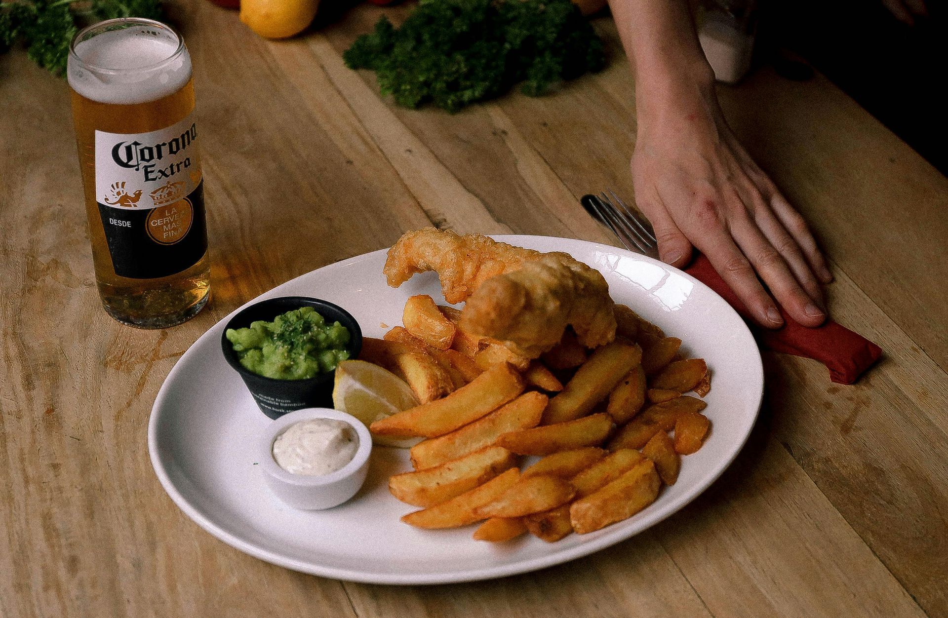 A person is reaching for a plate of fish and chips on a wooden table.