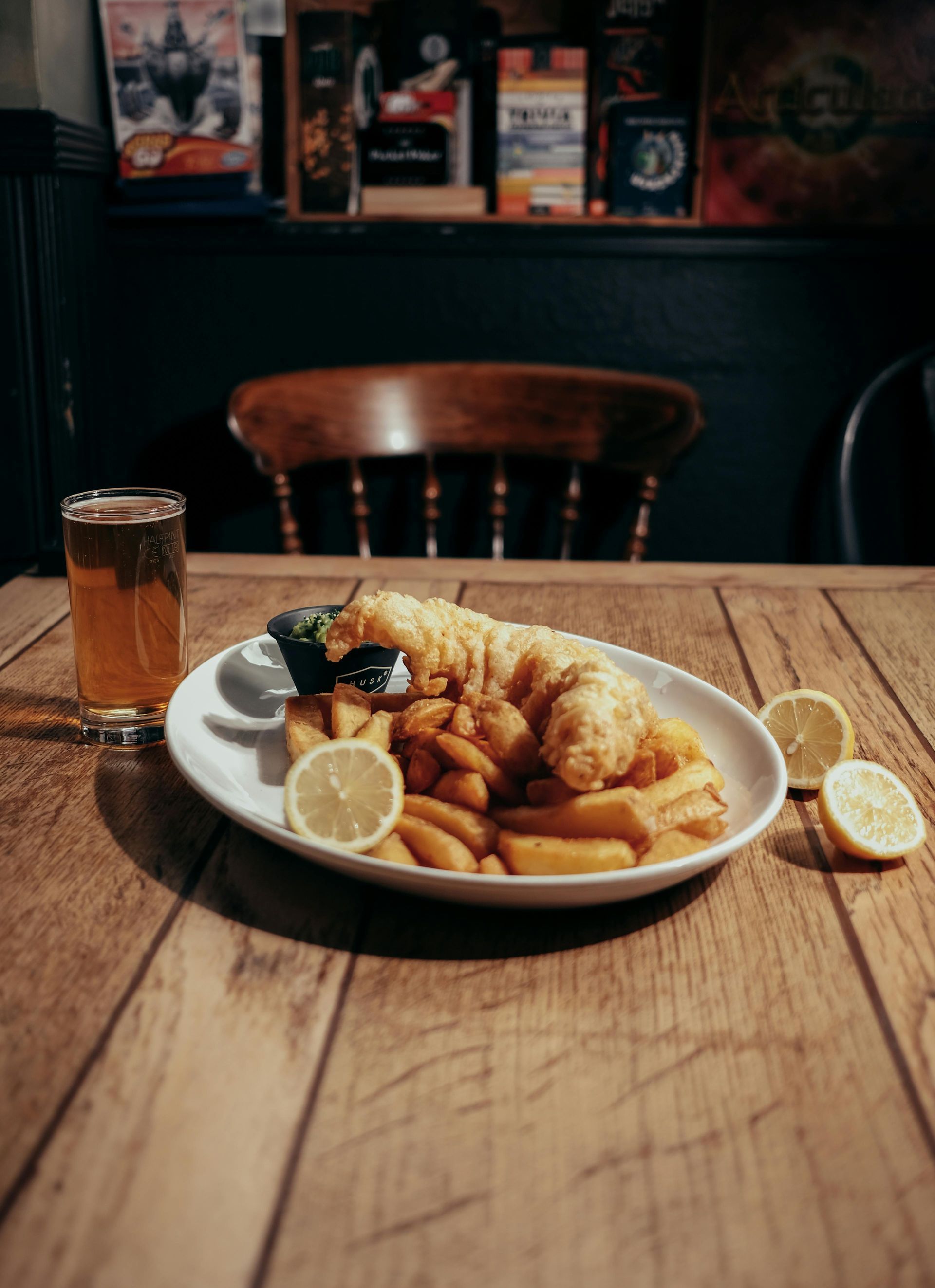 A plate of fish and chips on a wooden table next to a glass of beer.