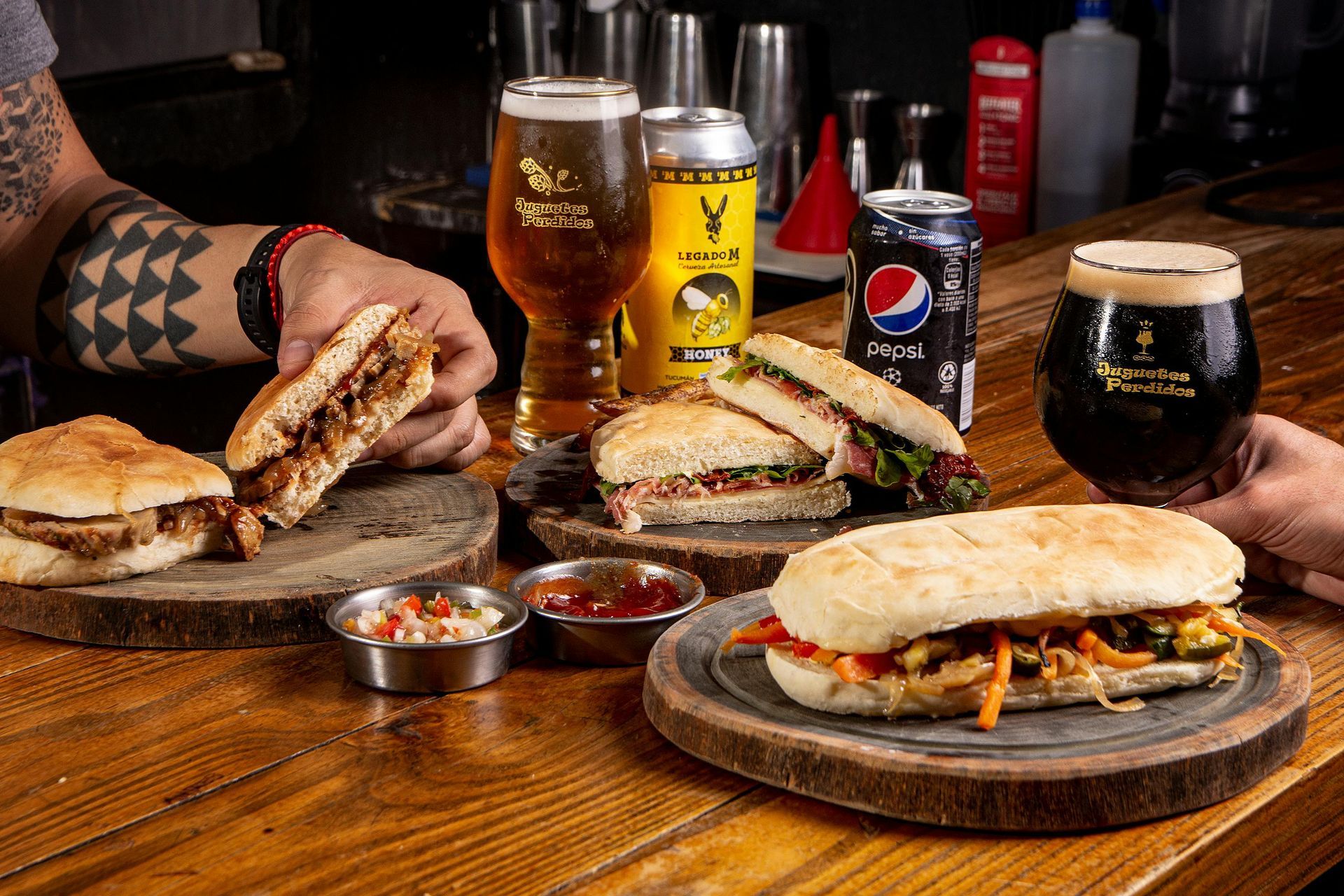 Two people are eating sandwiches and drinking beer at a bar.
