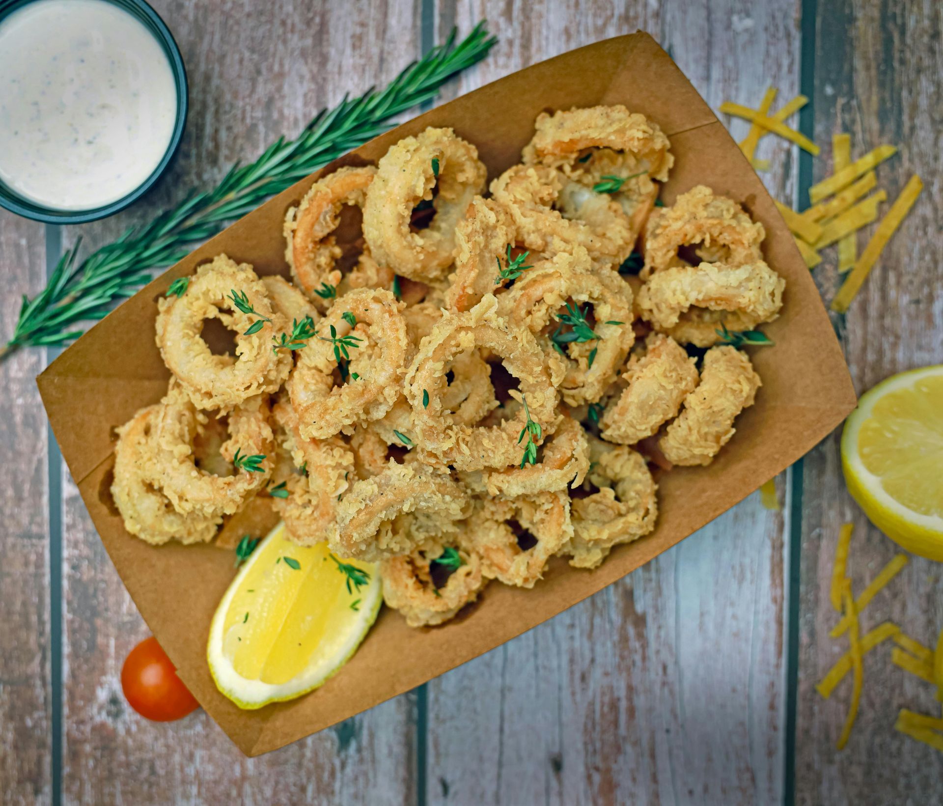 A tray of fried calamari with a lemon wedge on a wooden table.