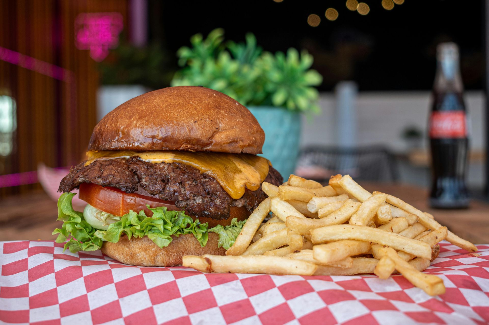 A hamburger and french fries on a checkered napkin on a table.