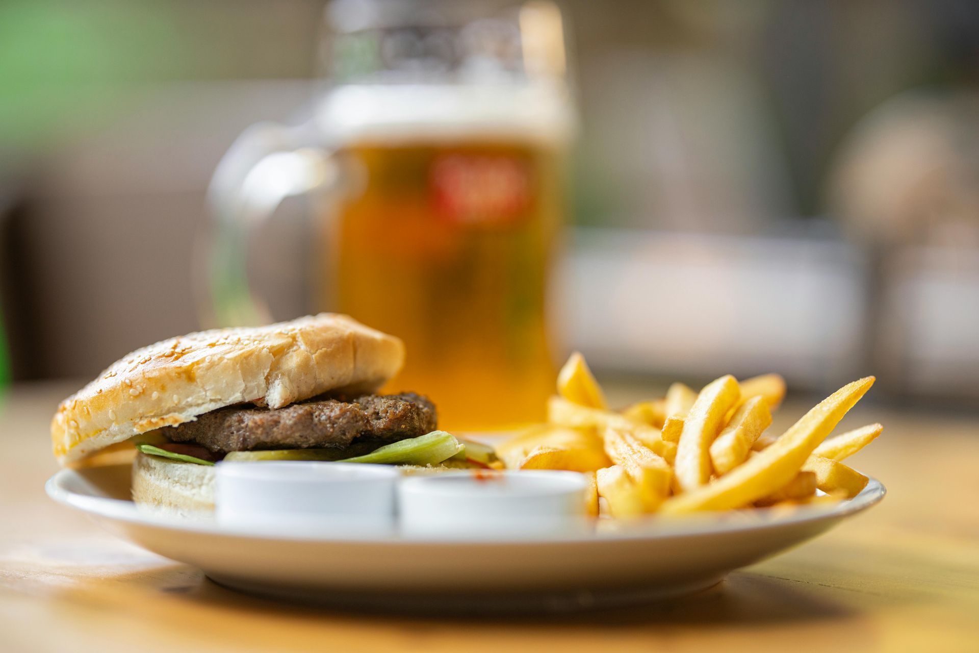 A hamburger and french fries on a plate with a glass of beer in the background.