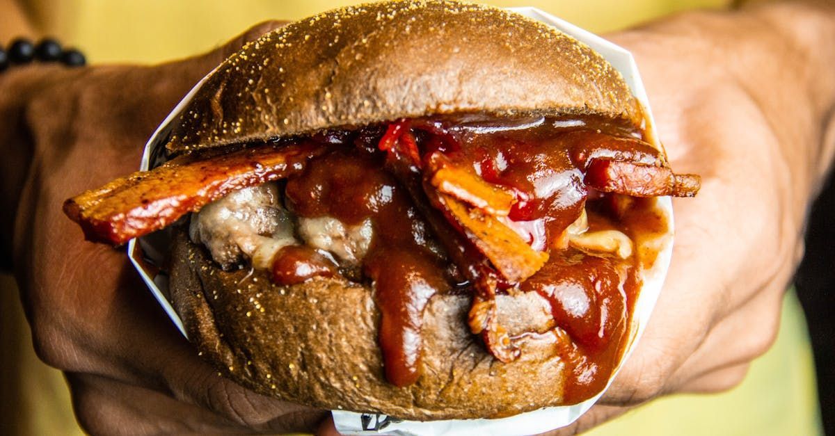 A person is holding a hamburger with bacon and sauce in their hands.