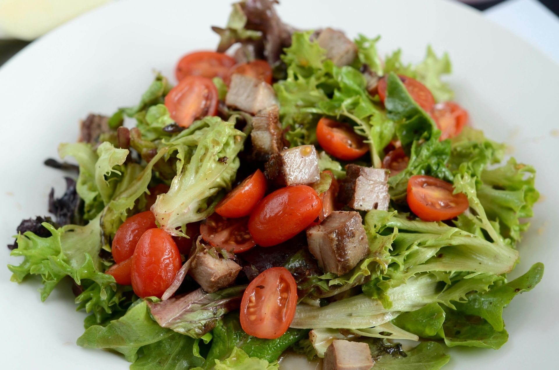 A salad with lettuce , tomatoes and meat on a white plate.