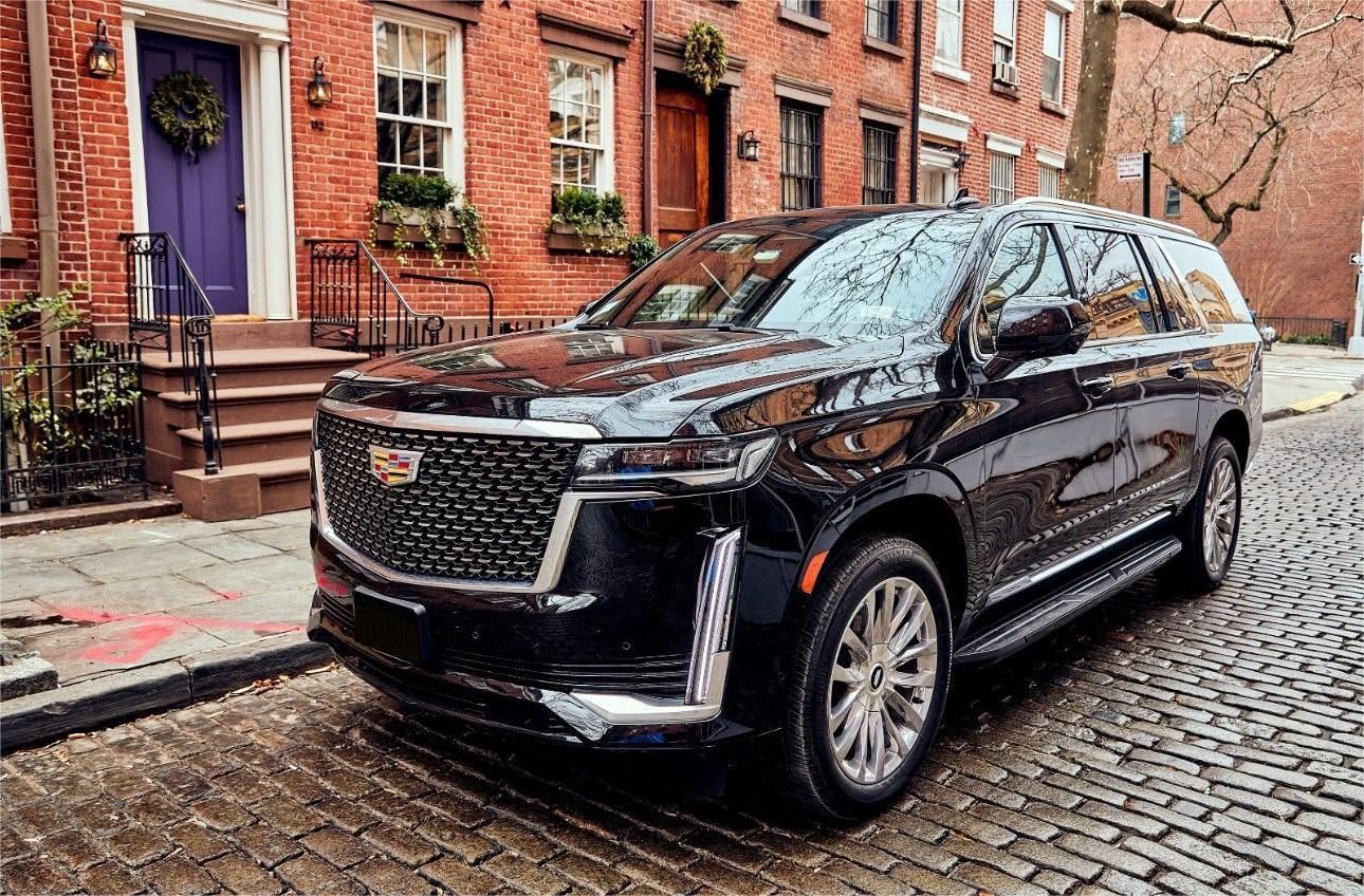 Black Cadillac Escalade parked on a cobblestone street in front of brick buildings with a purple door.
