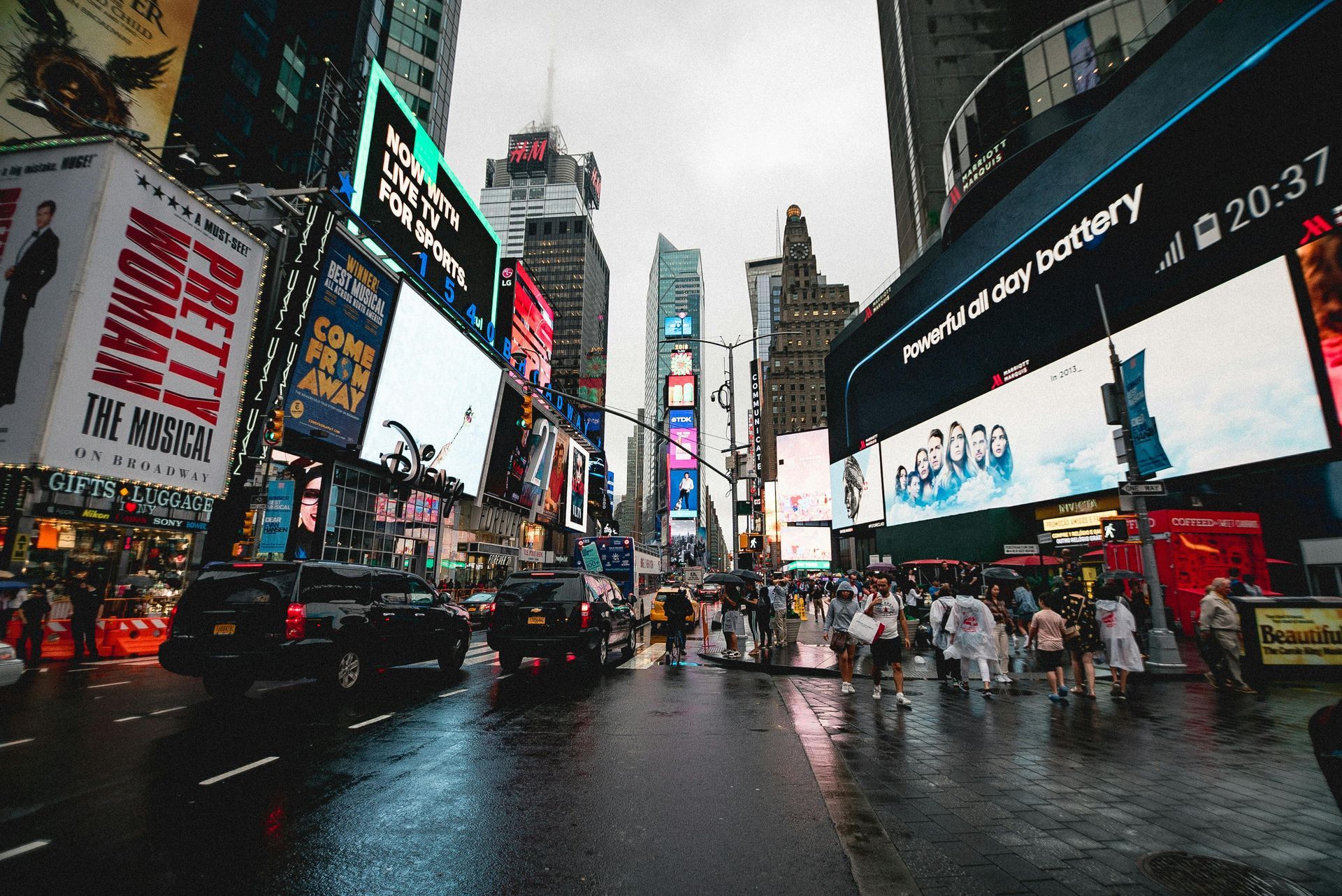 Times Square, NYC. Busy street with billboards, crowds, and wet pavement.