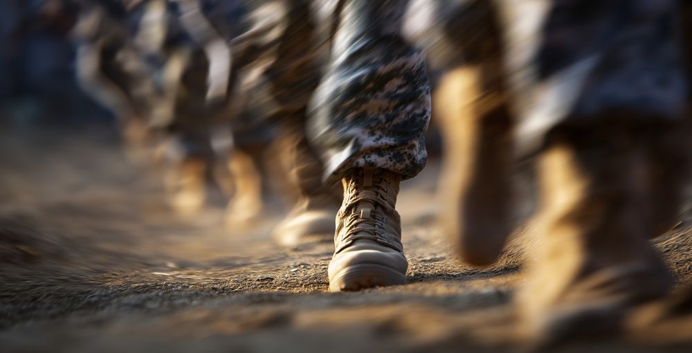 Soldiers marching in formation on a dirt path, focus on front boot.