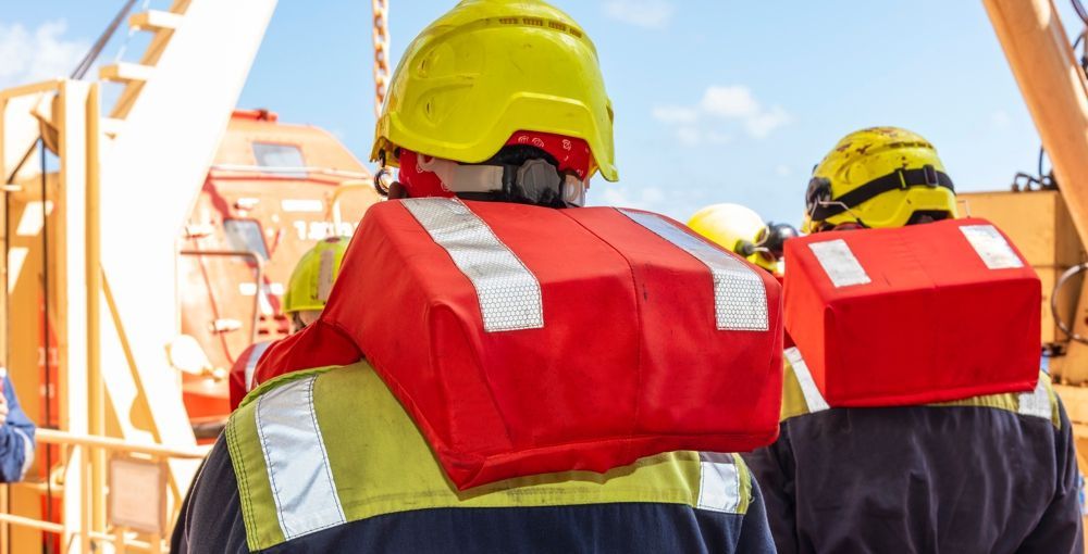 People wearing red life preservers and yellow hard hats on a ship deck.